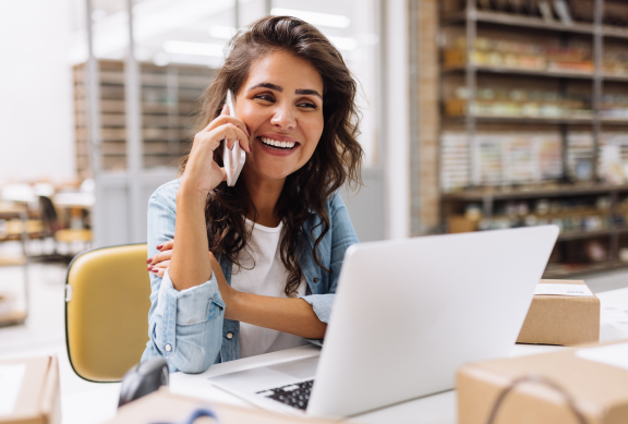 Happy female business owner on the phone looking at her laptop